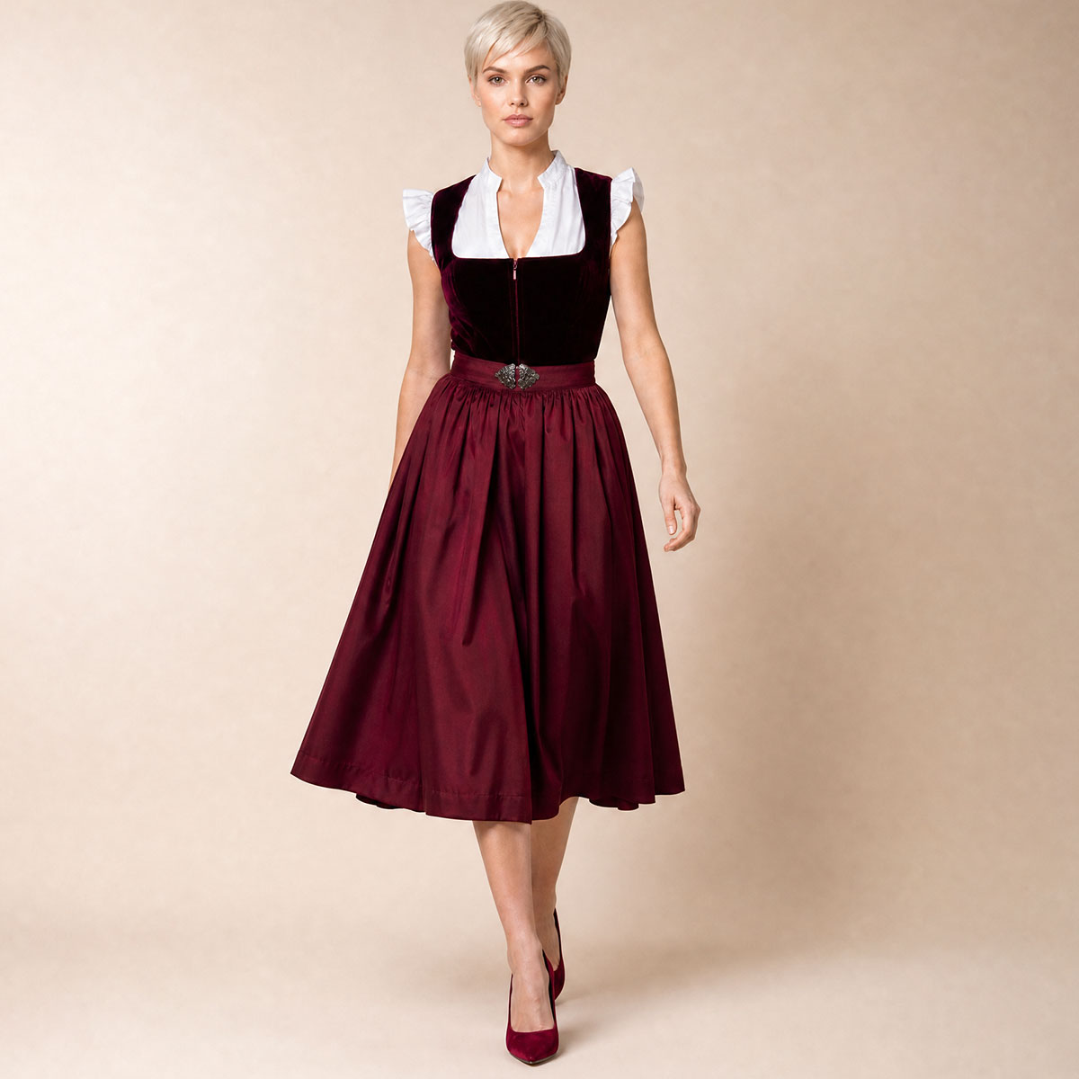 Studioaufnahme eines eleganten, dunkelroten Samtdirndls von Elli und Juliette mit einer weißen, rüschenärmeligen Bluse.